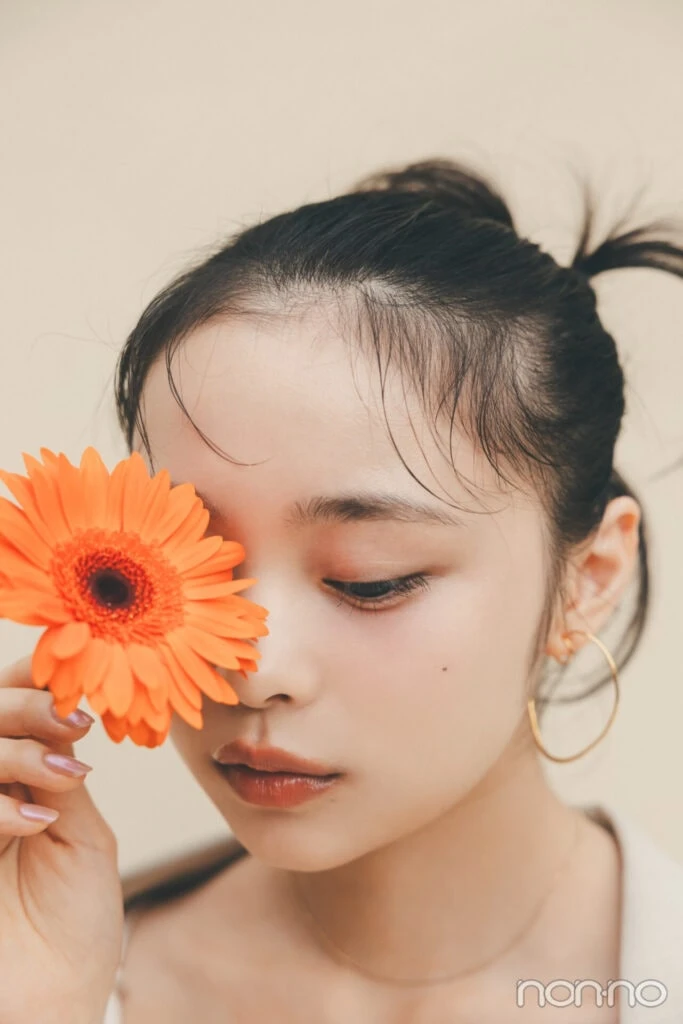 林芽亜里は、ガーベラで片目を隠しながら下を向いているカット
