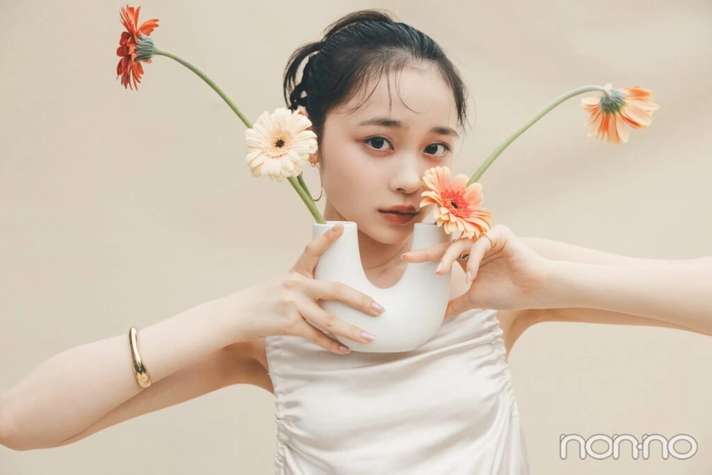 林芽亜里が、U字の花瓶に入ったガーベラを両手で持っているカット