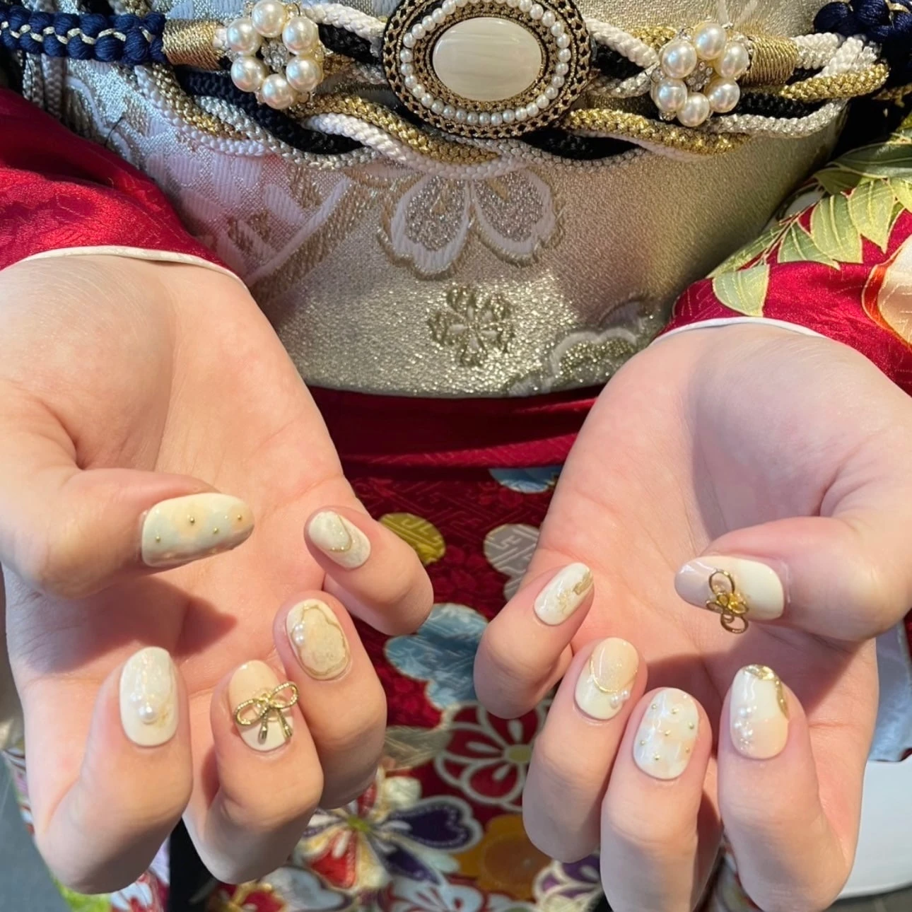 振袖を着た成人式ネイルの手元 白ベースでゴールドのリボンと水引パーツをつけたネイルデザイン