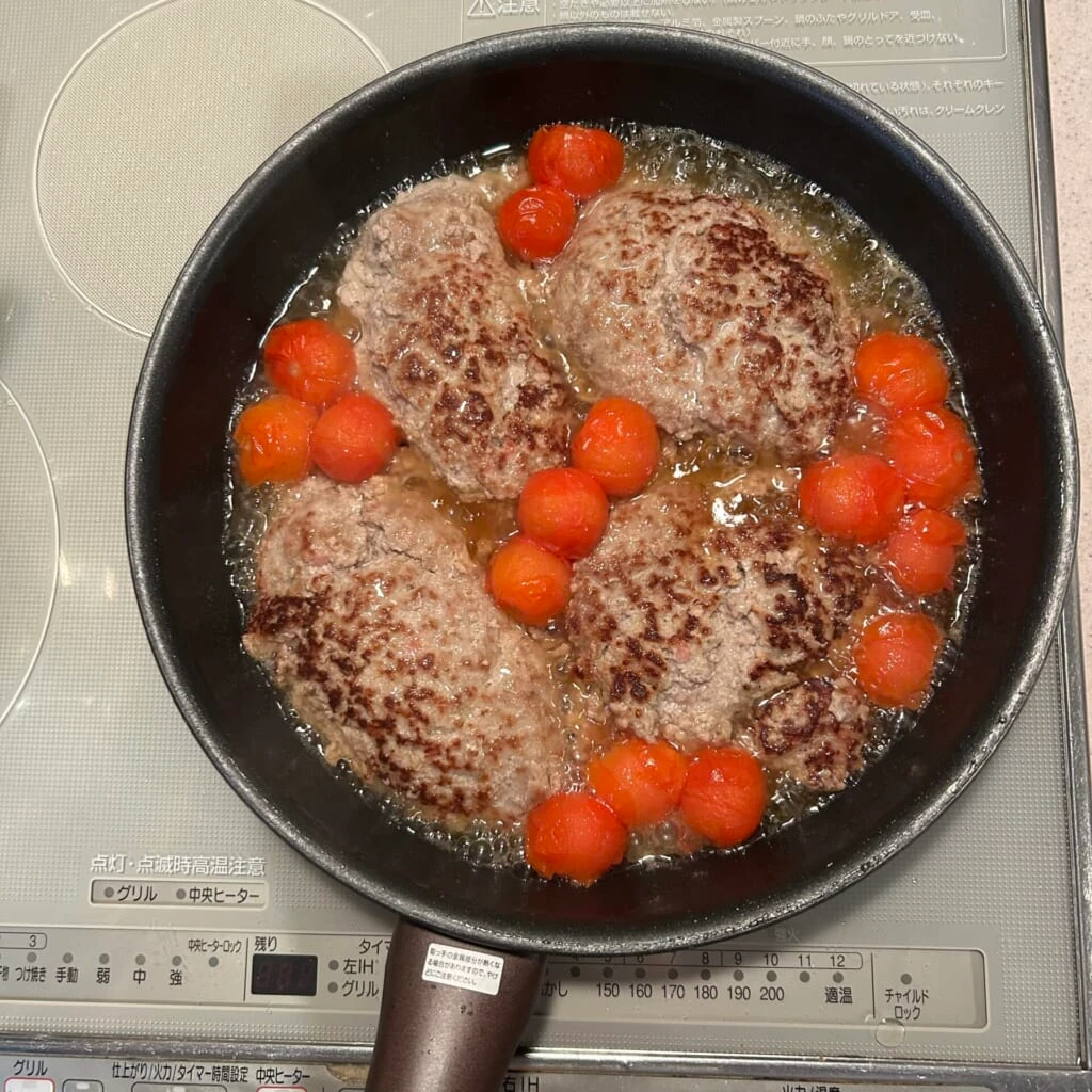 フライパンにハンバーグとトマトを入れて蒸している画像