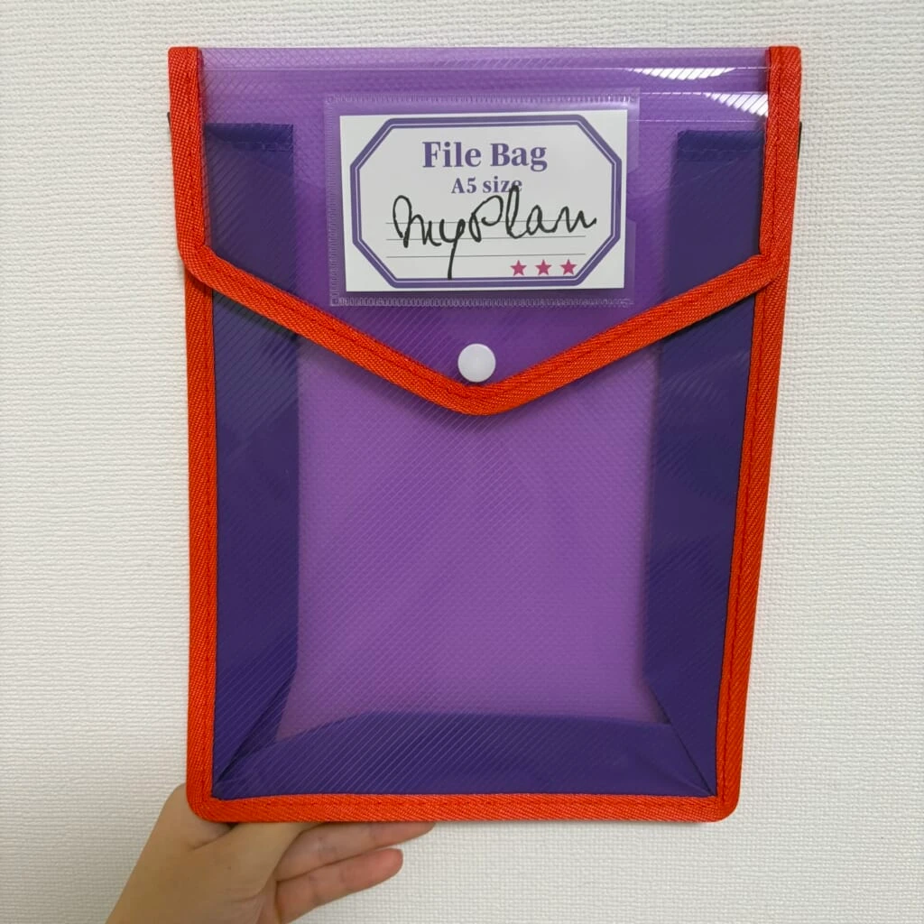 オレンジ色の縁取りとスナップボタンがついた紫色のファイルバッグ