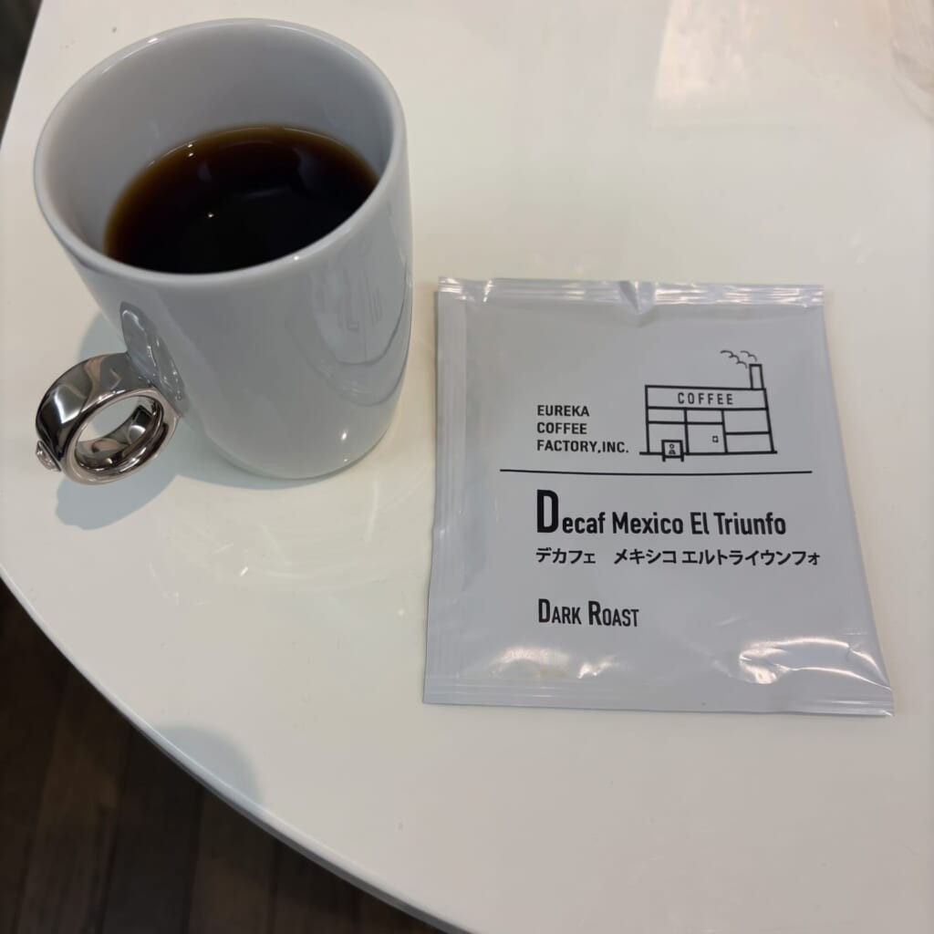 白いマグカップに淹れたデカフェコーヒーとエウレカコーヒーロースターズのパッケージ
