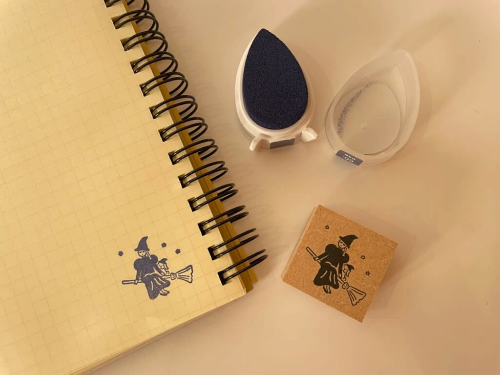 魔女のスタンプとスタンプ台を使ってノートにスタンプを押している