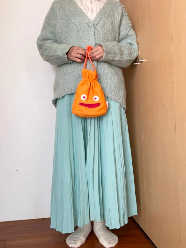緑色のカーディガン、スカートにストライプのシャツ。カルシファーのポーチを持っている