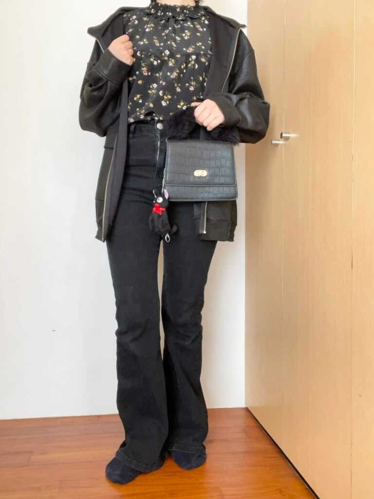 全身黒。レジャージャケット、花柄トップス、デニム、ミニバッグを合わせた服装