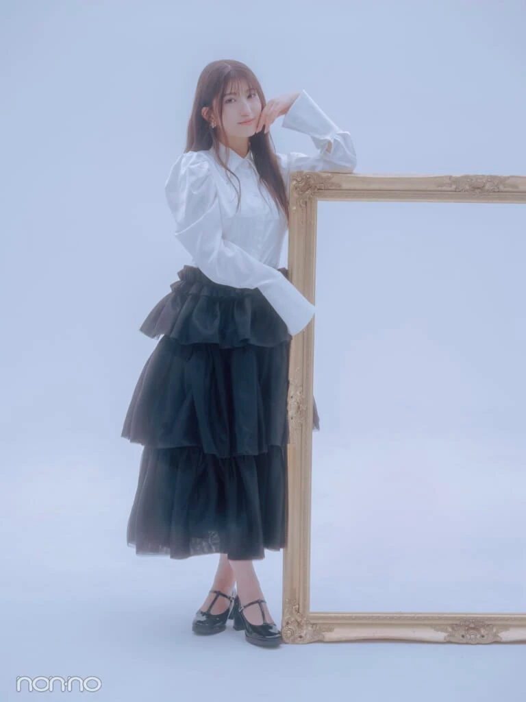 白いシャツと黒いティアードスカートを着て、大きな額縁にもたれるモーニング娘。’25羽賀朱音さんの全身カット