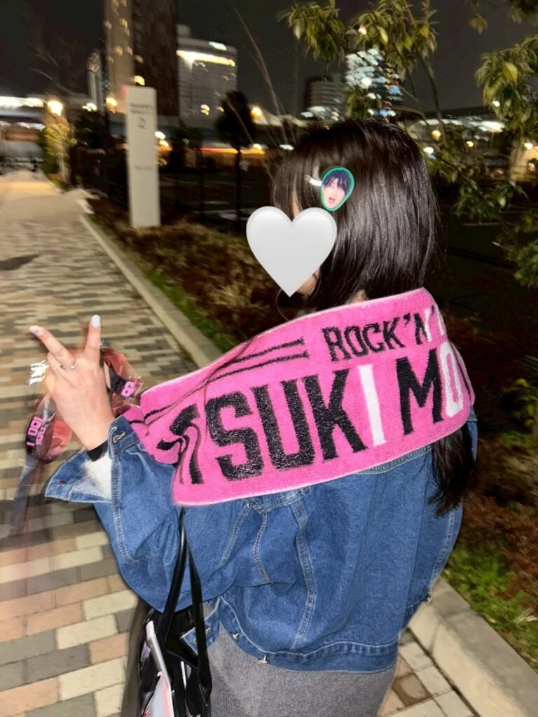 帰り道に撮影してもらった後ろ姿。髪には推しのヘアピン、推しの名前入りのピンクのタオルを肩にかけ、手には銀テープを持っている。