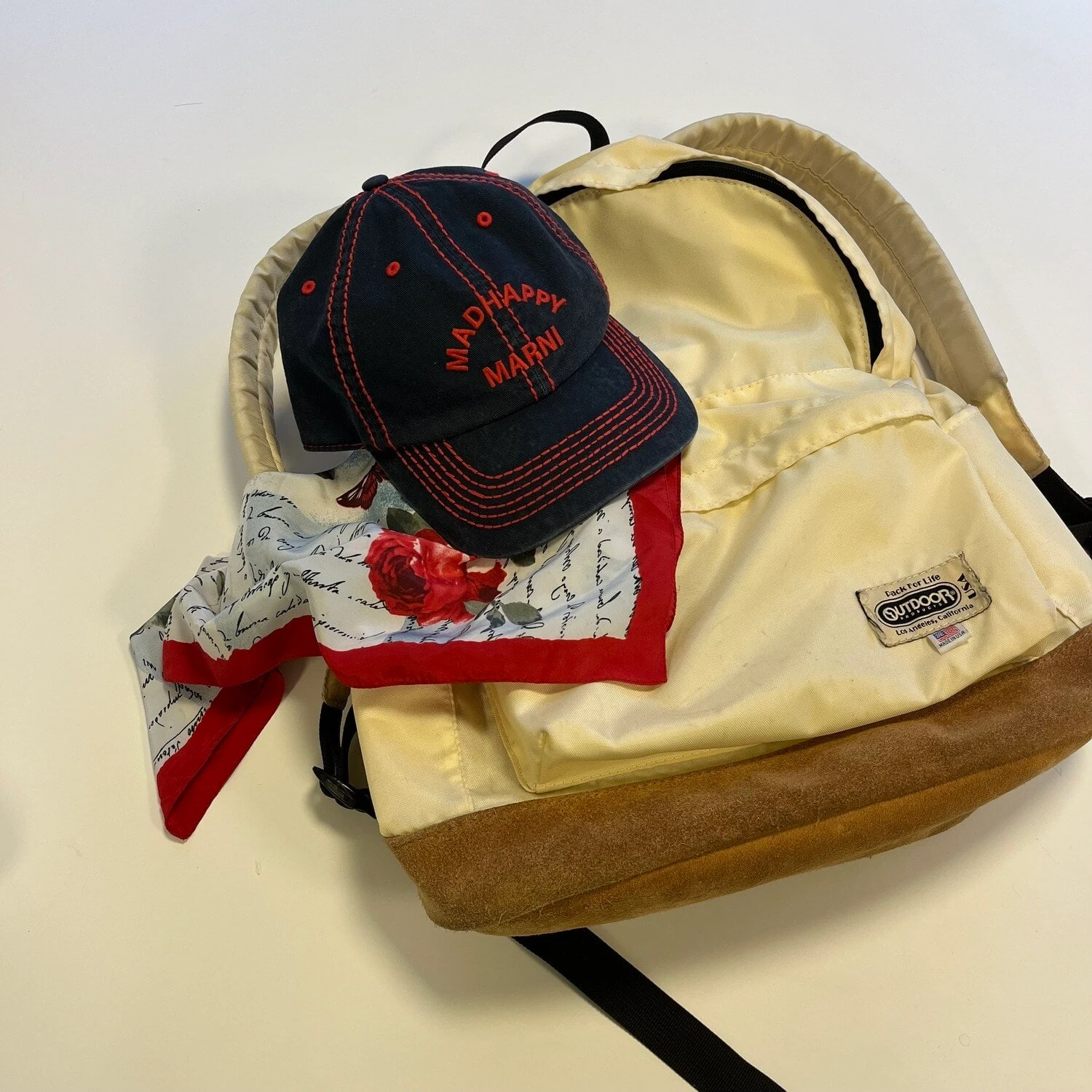 机に置かれたOUTDOOR PRODUCTSの白いデイパックとMARNIのキャップ