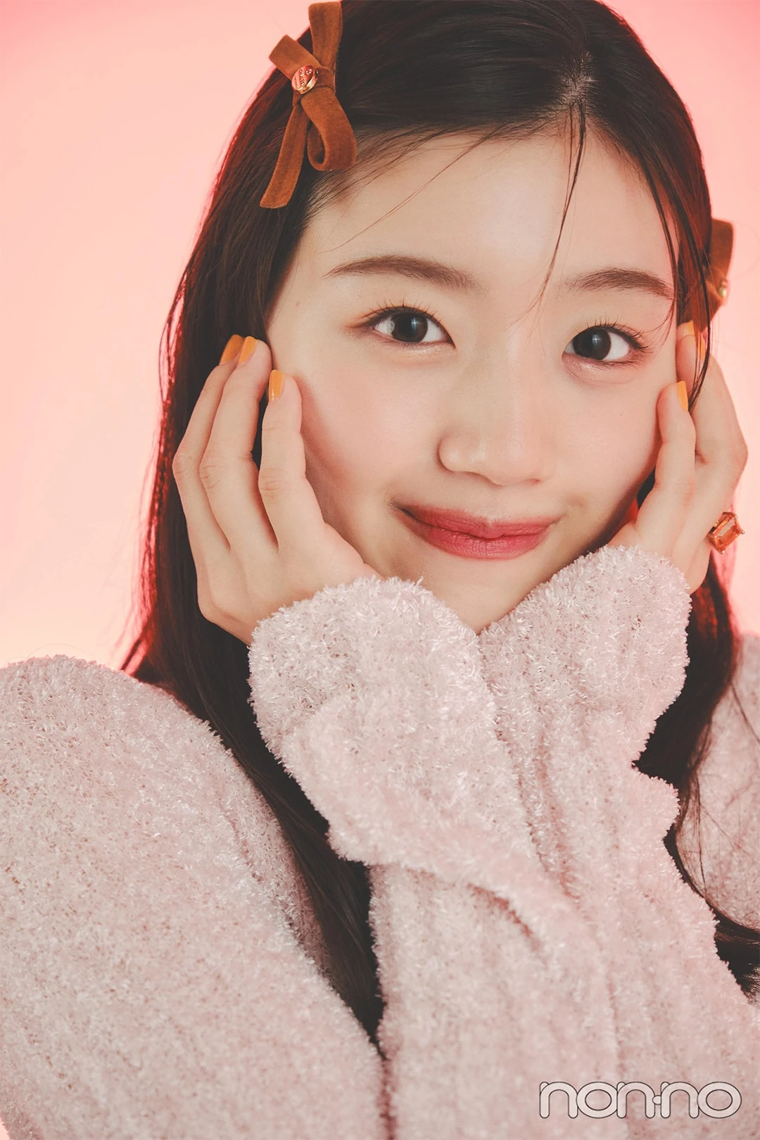 ピンクのニットを着て両手で頬を包む佐々木美玲